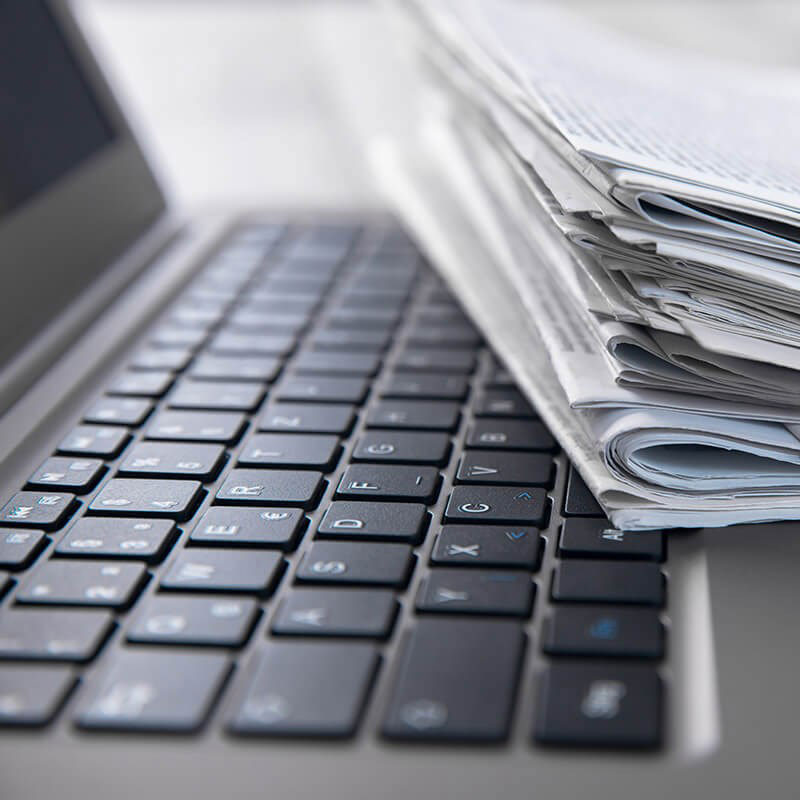 The image shows a laptop keyboard with papers resting on top, suggesting multitasking or workload management.