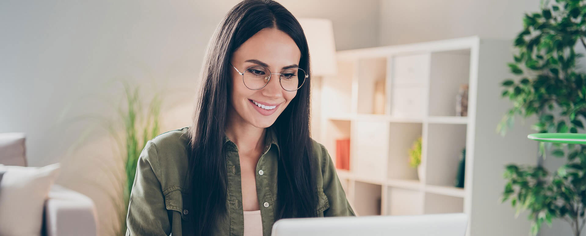A woman sitting at a desk with a laptop, smiling towards the camera.