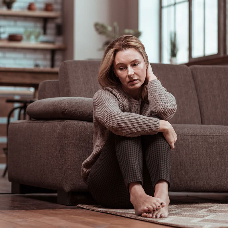 A woman sitting on a couch with her feet up, wearing a sweater and looking downwards.
